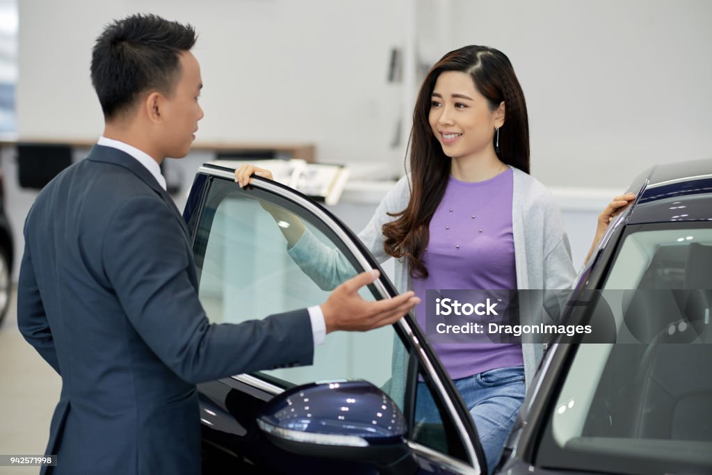 Selling cars Salesman showing car to beautiful young Asian woman Asian and Indian Ethnicities Stock Photo