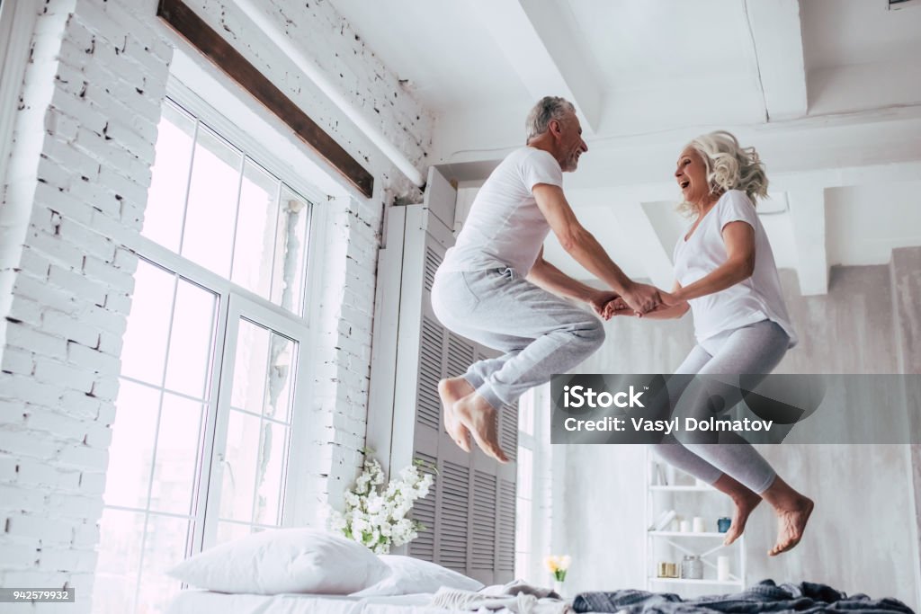 Senior couple at home Love lives forever! Senior couple at home. Handsome old man and attractive old woman are enjoying spending time together. Having fun and jumping in bed. Jumping Stock Photo