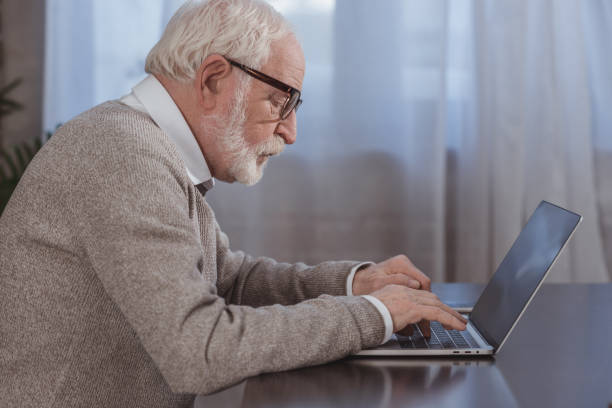 istock side view of handsome grey hair man using laptop at home 942588320