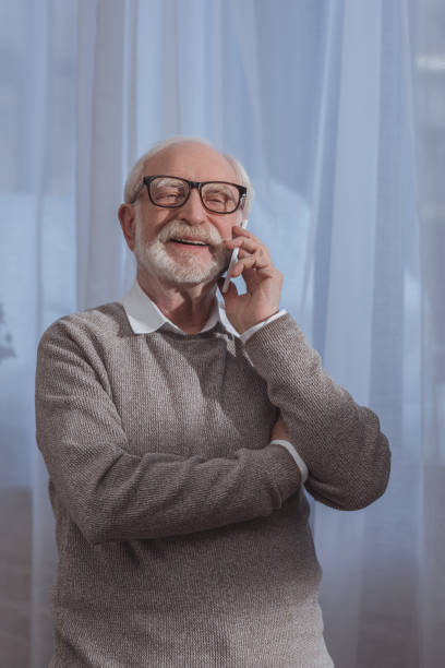 istock handsome smiling grey hair man talking by smartphone at home 942588442