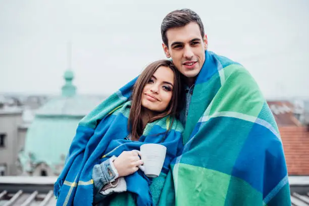 Beautiful couple in love on the balcony, covered with a blanket and drinking coffee