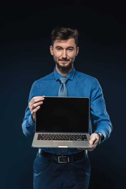 istock Young businessman holding laptop with blank screen isolated on blue 942602714