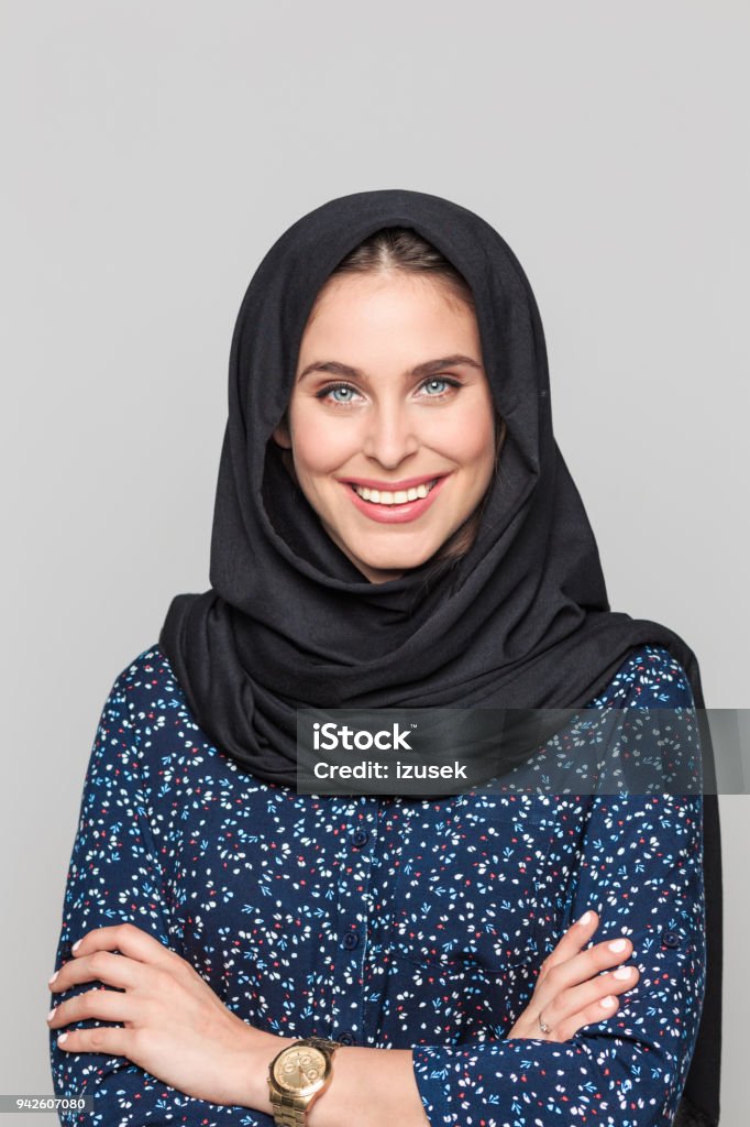 Portrait of cheerful young muslim woman Portrait of cheerful young muslim woman. Businesswoman in hijab looking at camera against grey background. Gray Background Stock Photo