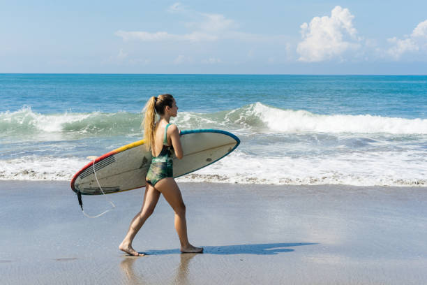 istock young female surfer walking with surfboard on beach at the sea 942607202