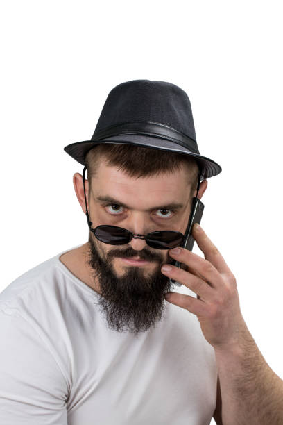 istock Serous bearded  man in hat and glasses talking on the phone isolated on white background with copy space 942607708