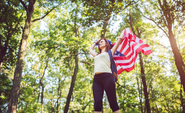 istock Woman with backpack holding american flag in forest. 942607852
