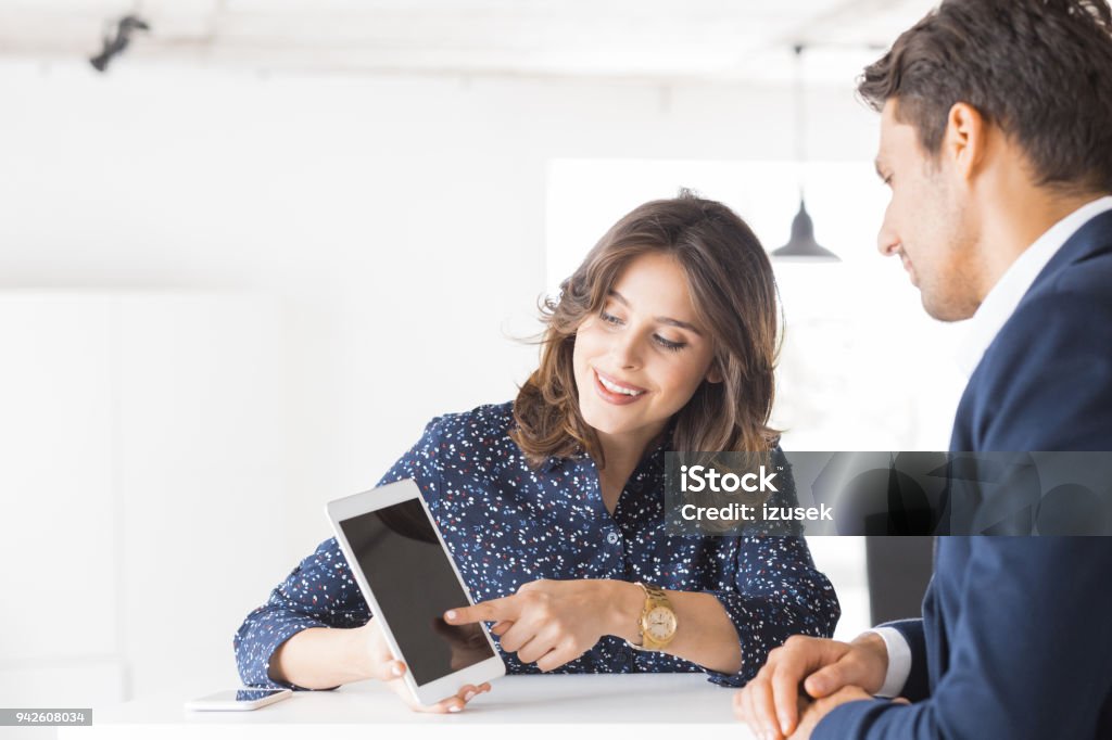 Two business people working together in office Smiling woman showing a proposal on digital tablet to businessman. Two business people working together at office using digital tablet. Analyzing Stock Photo