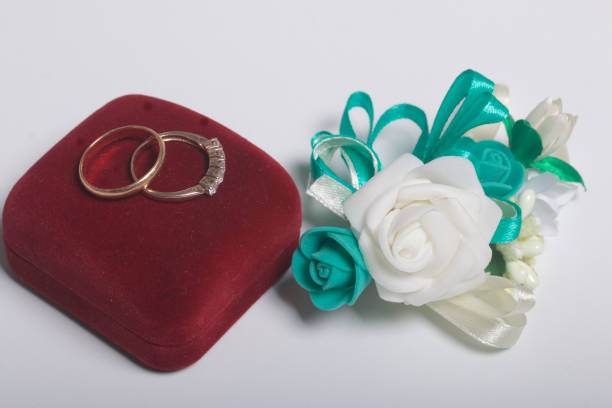 Wedding decor. Boutonniere groom, their wedding rings on box, lie on a white surface.