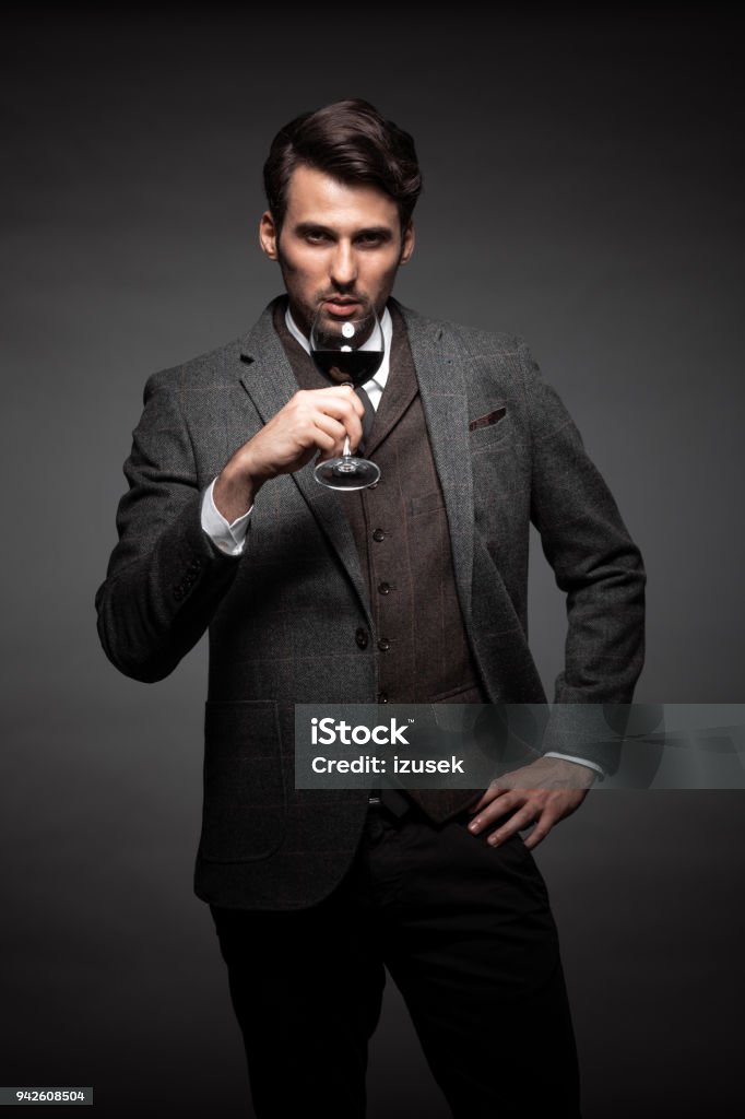 Handsome young man with a glass of wine Portrait of handsome young man in suit holding a glass of wine on black background Fashionable Stock Photo