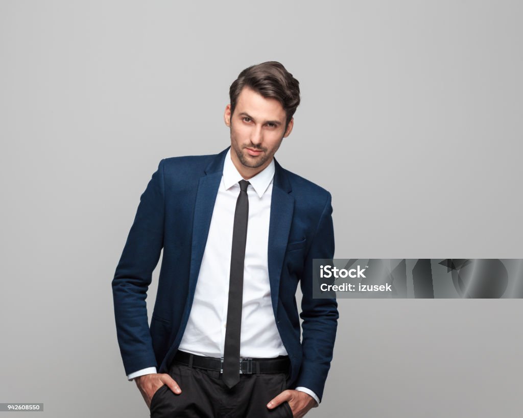Portrait of elegant young man in suit Portrait of elegant young man in suit standing against grey background. Suit Stock Photo