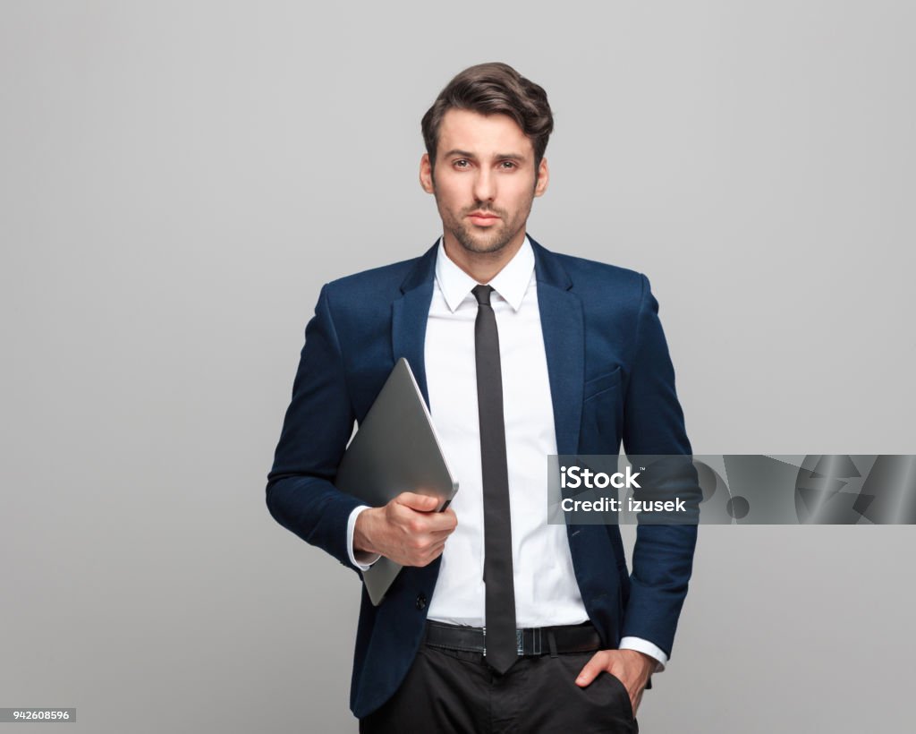 Confident and handsome businessman holding laptop Portrait of handsome businessman holding digital tablet standing against grey background and looking at camera. Laptop Stock Photo
