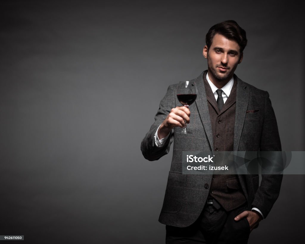 Handsome young man with a glass of wine Portrait of handsome young man in suit holding a glass of wine on black background. Men Stock Photo