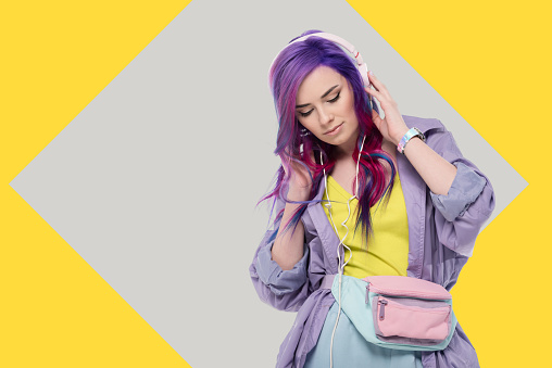 stylish young woman with colorful hair in purple trench coat listening music with headphones