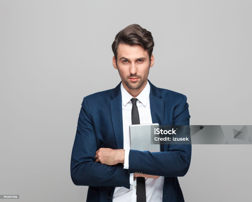 Handsome businessman holding digital tablet Portrait of handsome businessman holding digital tablet standing against grey background and looking at camera. Adult Stock Photo