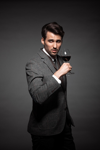 Portrait of handsome young man in suit holding a glass of wine on black background