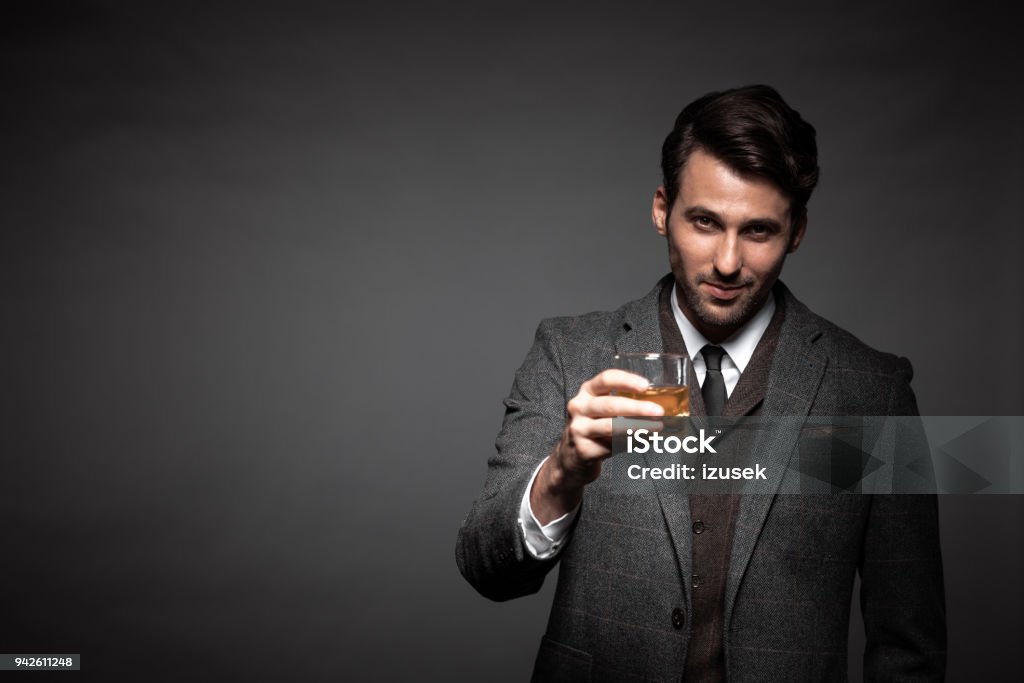 Portrait of handsome man drinking whiskey Portrait of handsome man drinking whiskey in studio. Business man with glass of whiskey looking at camera on black background. Whiskey Stock Photo