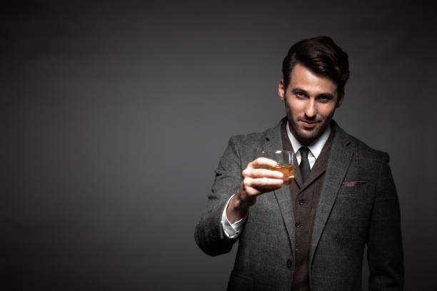 Portrait of handsome man drinking whiskey Portrait of handsome man drinking whiskey in studio. Business man with glass of whiskey looking at camera on black background. charming stock pictures, royalty-free photos & images