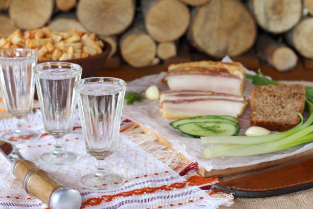 A glass of vodka and a lard on the background of woodpile  of firewood.