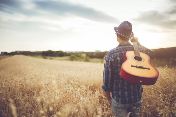 istock Man walking through the wheat field with guitar on back. 942612678