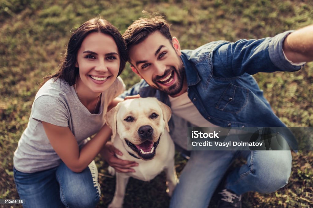 Couple with dog Beautiful romantic couple is having fun with their dog labrador retriever outdoors. Sitting on a green grass and making selfie. Dog Stock Photo