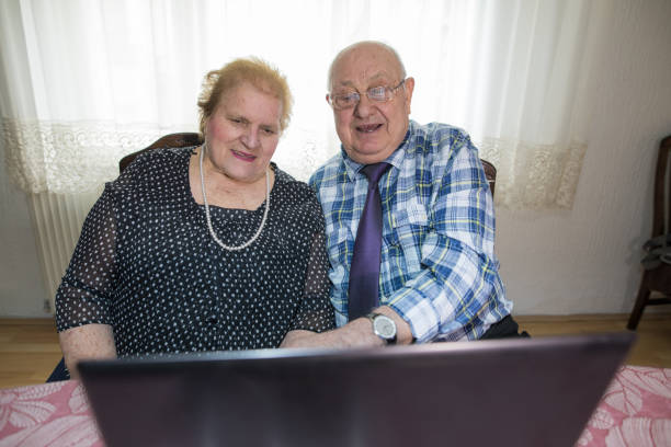 sechzig jahre zusammen. älteres paar mit laptop zu hause - overweight smiling senior women 70s stock-fotos und bilder