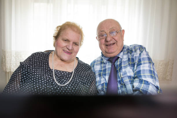 sechzig jahre zusammen. älteres paar mit laptop zu hause - overweight smiling senior women 70s stock-fotos und bilder