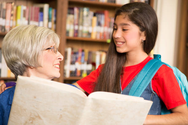 istock Teacher, librarian reads book to elementary student in library or classroom. 942654434