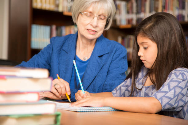 istock Teacher, mentor helps elementary-age schoolgirl with homework. 942654834