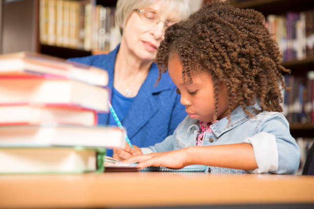 istock Teacher, mentor helps elementary-age schoolgirl with homework. 942655212