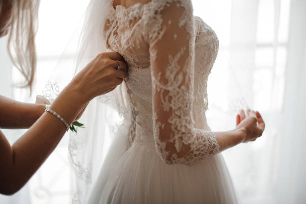 Bridesmaid making bow-knot on the back of brides wedding dress Bridesmaid making a bow-knot on the back of brides lacy white and beautiful wedding dress wedding dress stock pictures, royalty-free photos & images