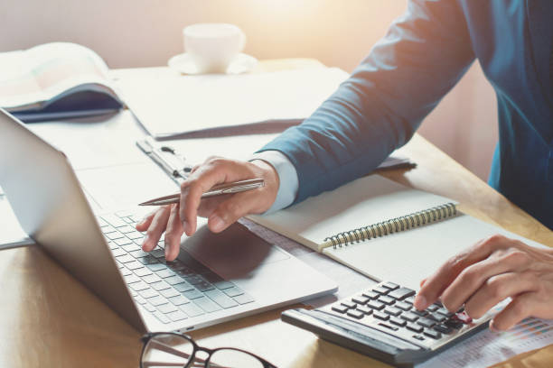 бизнесмен, работающий в офисе с использованием калькулятора и ноутбука. концептуальное финансирование и бухгалтерский учет - hand calculator стоковые фото и изображения