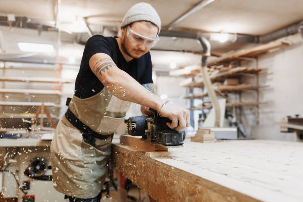 istock Carpenter working with electric planer on wooden plank in workshop. Craftsman makes own successful small business. 942689632