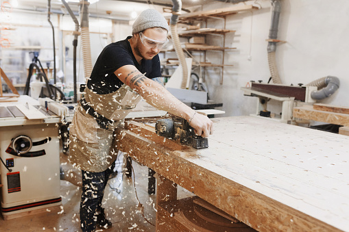Trabajar con el cepillo eléctrico sobre tablón de madera en el taller del carpintero. Artesano hace negocio pequeño éxito propio. photo