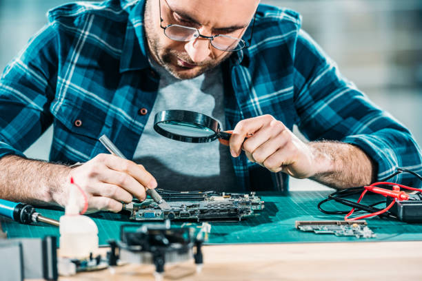istock Repairman looking through magnifying glass while fixing circuit board 942692634