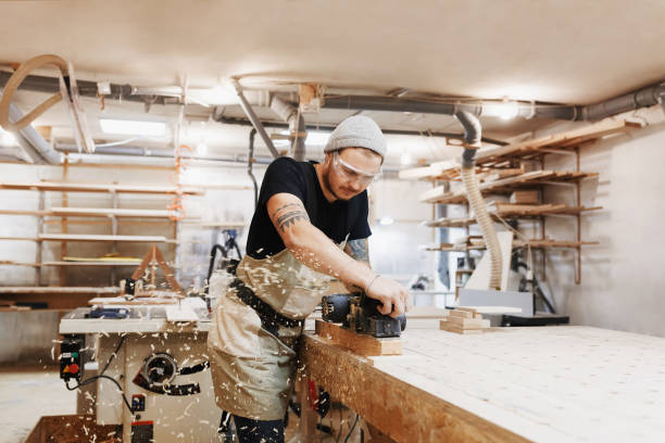 istock Carpenter working with electric planer on wooden plank in workshop. Craftsman makes own successful small business. 942692704