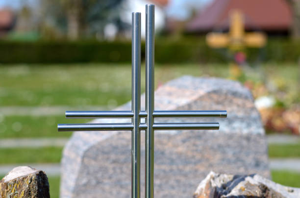 Simple metal cross with no name on a grave in a cemetery with colorful flowers in a close up view