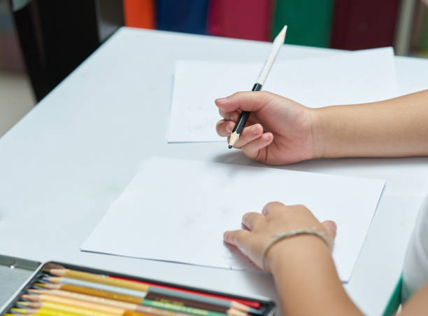 istock Kid Hands holds color pencil and think about writing things on white blank papers on desk or study table 942720668