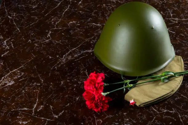 Photo of military helmet, carnations and a pilot's cap, against the background of the monument