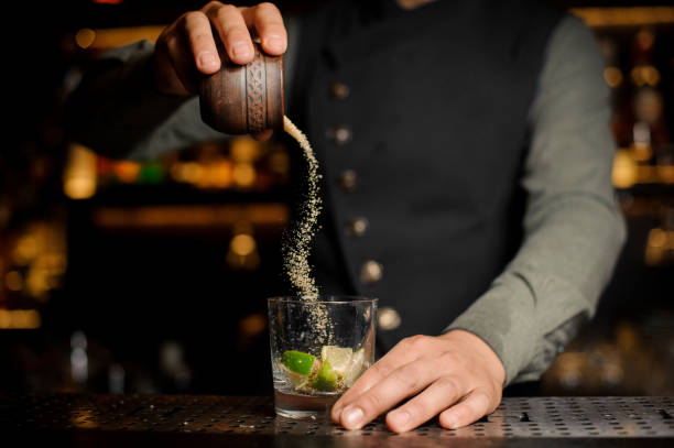 бармен добавляет тростниковый сахар в коктейльный бокал с лаймом. процесс приготовления коктейля кайпиринья - turbinado sugar стоковые фото и изображения