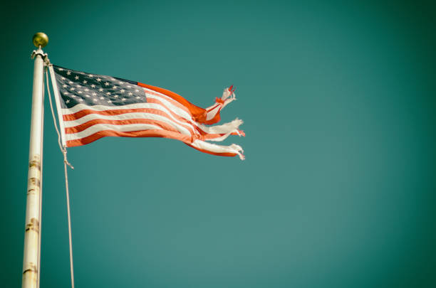 Tattered American flag flying on rusted flagpole in faded blue sky