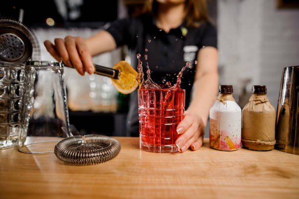 feat barmaid adding to the cocktail glass slice of lemon using tongs feat blonde barmaid in black shirt adding to the cocktail glass slice of lemon using tongs at the bar counter cocktail bar busy stock pictures, royalty-free photos & images
