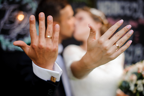 Blurred figures of happy and smiling bridegroom and bride kissing and showing wedding rings on their fingers