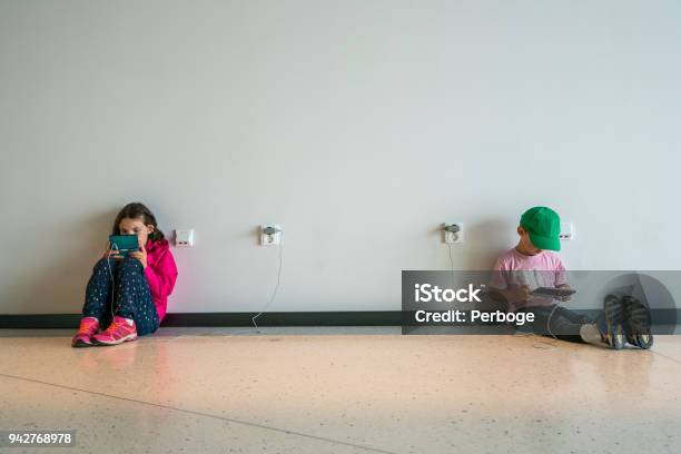 Two Children Boy And Girl Sitting On A Floor Concentrating And Playing Electronic Games Stock Photo - Download Image Now