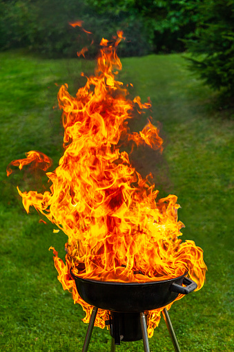 A big fire flashover a black grill outdoors when having a barbecue. Vertical composition.