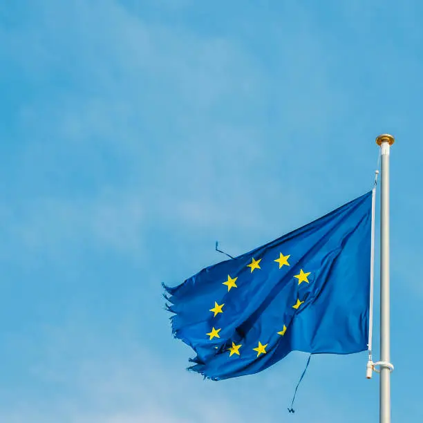 European Union flag on a mast proudly moving in the wind despite the ripped up pieces of cloth on the edges, which is perhaps a metaphor for the serious crisis currently facing the economic block.