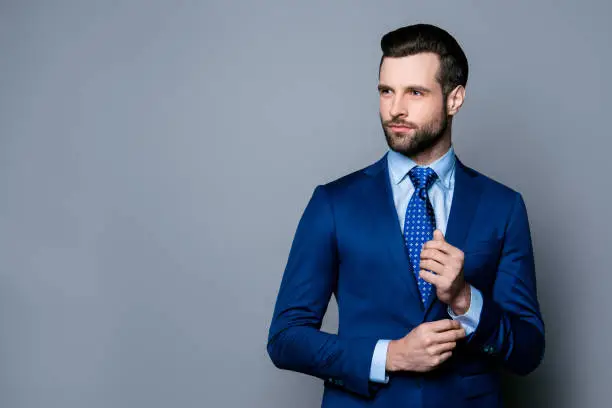 Photo of Portrait of serious fashionable handsome man in blue suit and tie  buttoning cufflinks