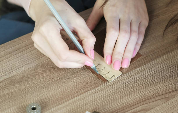 istock Seamstress measures segments on leather fabric with pencil and ruler, woman's hands close-up. 942796382