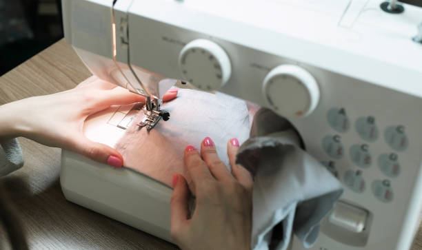 istock Woman sewing light fabric on a sewing machine close-up. Side view. 942796686