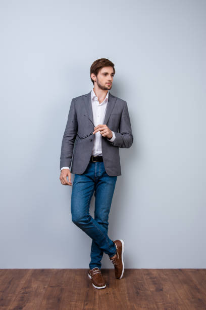 istock Handsome young man with bristle in casual clothes holding spectacles and posing. Successful stylish entrepreneur wearing jacket, jeans and shoes 942803342