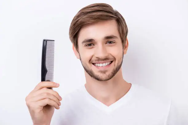 Photo of Portrait of handsome cheerful bearded young man showing his black comb while standing white background
